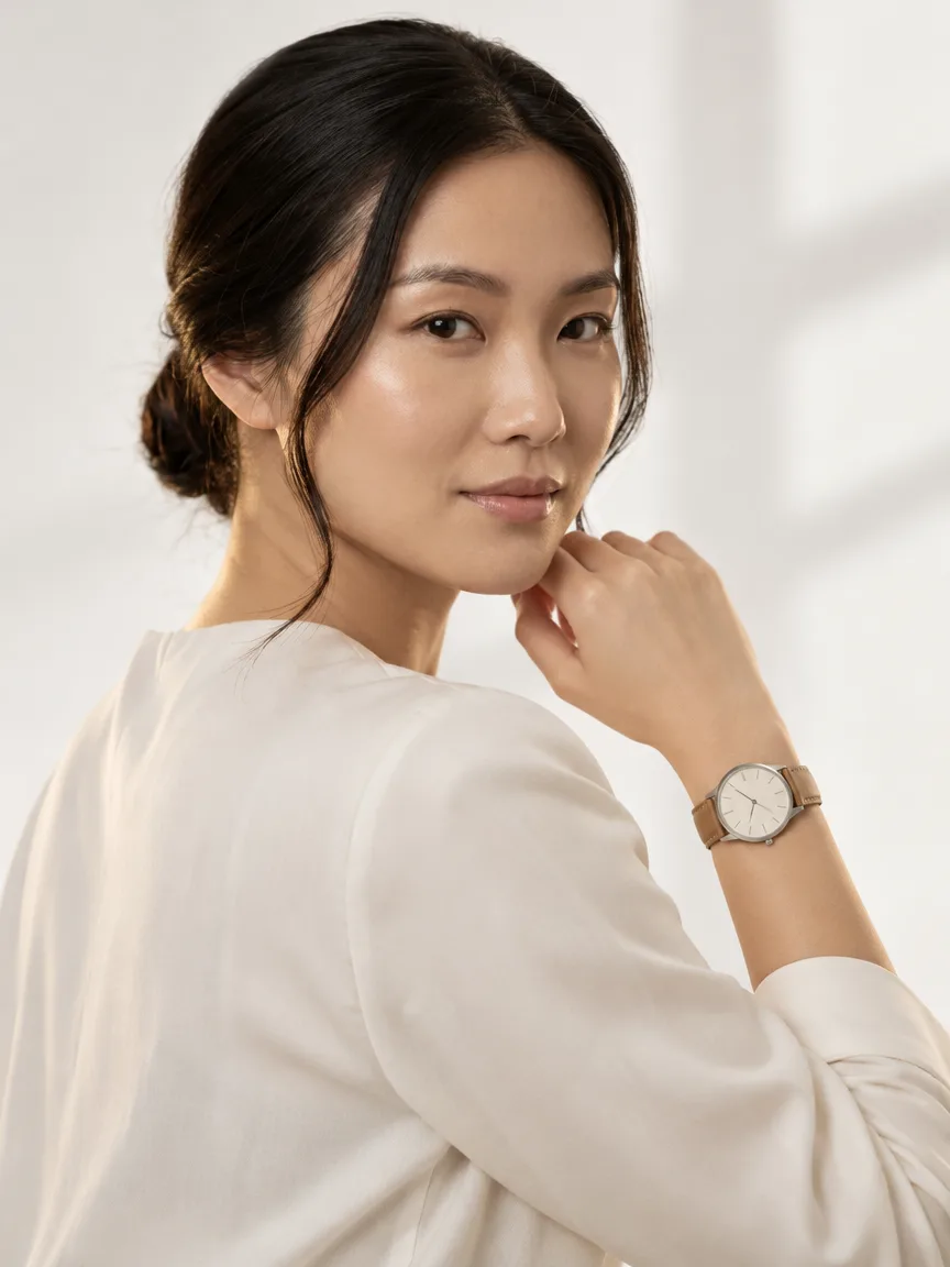 AI-generated model wearing a stainless-steel watch with a cream dial and tan leather strap, over-the-shoulder view from behind